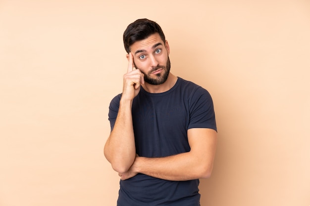 Homem bonito caucasiano na parede bege, pensando uma idéia