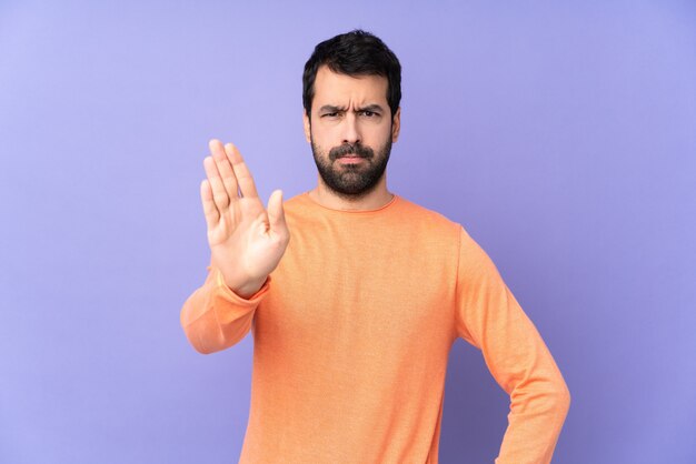 Homem bonito caucasiano sobre isolado roxo fazendo o gesto de parada