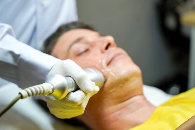 Homem bonito closeup tendo terapia para estimular a pele facial e tratamento ultrassônico facial pelo bem-estar cosmetologista profissional