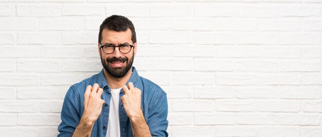 Homem bonito com barba ao longo da parede de tijolo branco frustrado por uma situação ruim