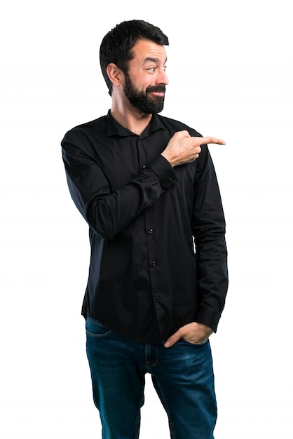 Foto homem bonito com barba, apontando para a lateral no fundo branco