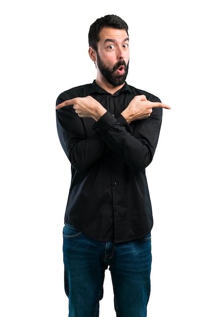 Foto homem bonito com barba apontando para as laterais com dúvidas sobre fundo branco