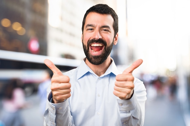 Homem bonito com barba com o polegar para cima em fundo não focado