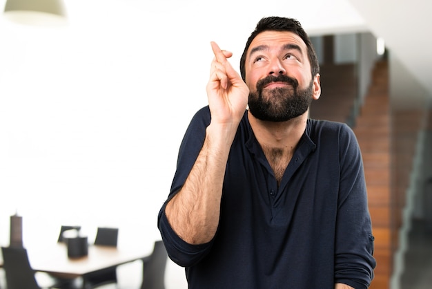 Homem bonito com barba com os dedos cruzados dentro da casa