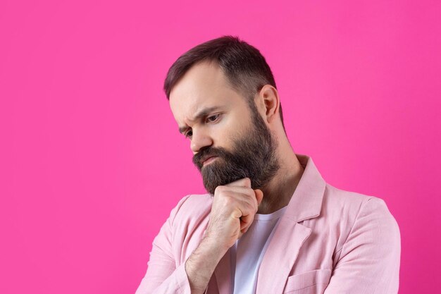 Homem bonito com barba em uma jaqueta rosa está pensando sobre um fundo vermelho isolado