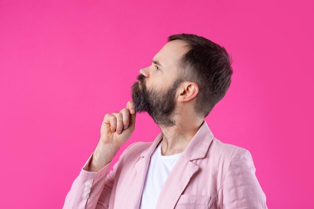 Homem bonito com barba em uma jaqueta rosa está pensando sobre um fundo vermelho isolado