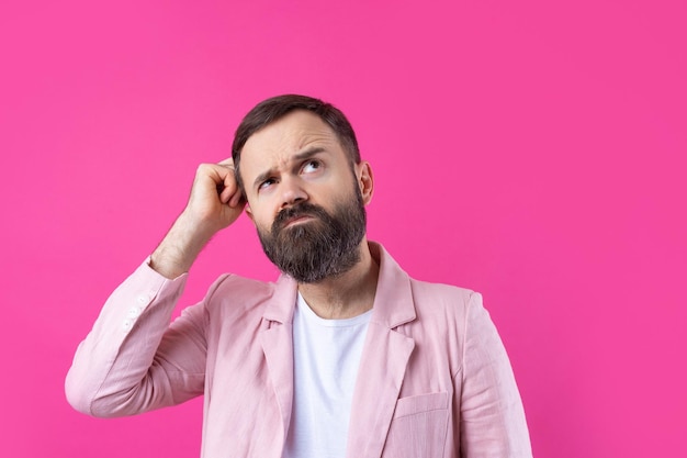 Homem bonito com barba em uma jaqueta rosa está pensando sobre um fundo vermelho isolado