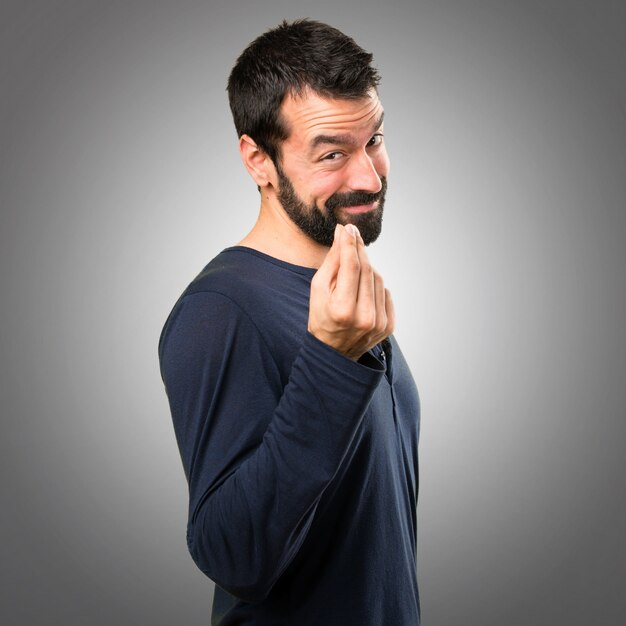 Homem bonito com barba fazendo gesto de dinheiro em fundo cinza