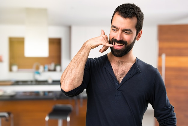 Foto homem bonito com barba fazendo gesto de telefone dentro da casa