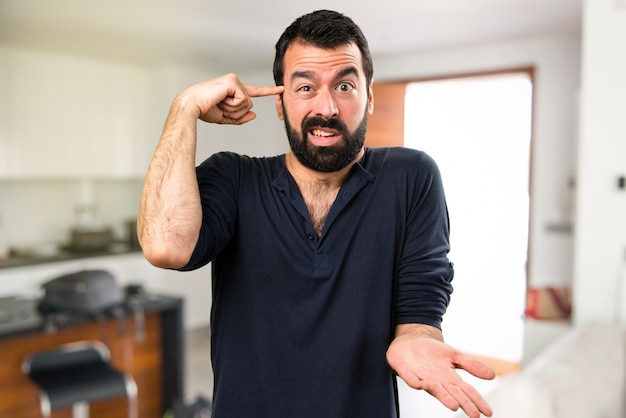 Homem bonito com barba fazendo um gesto louco dentro da casa