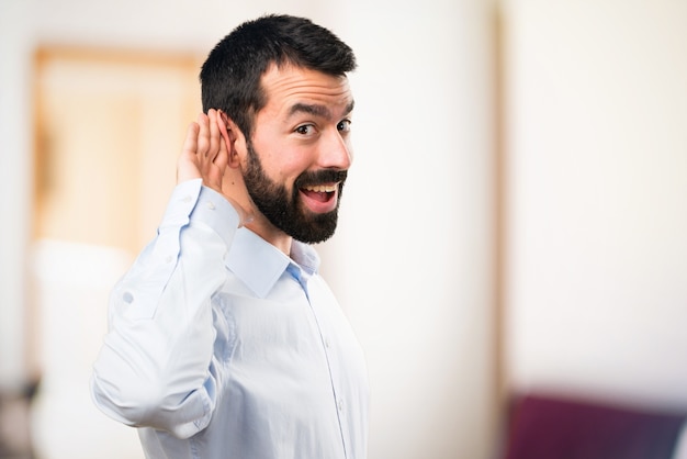 Homem bonito com barba ouvindo algo em fundo não focado