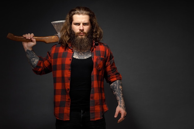 Homem bonito com cabelo comprido, com um machado nas mãos em um fundo escuro do estúdio.