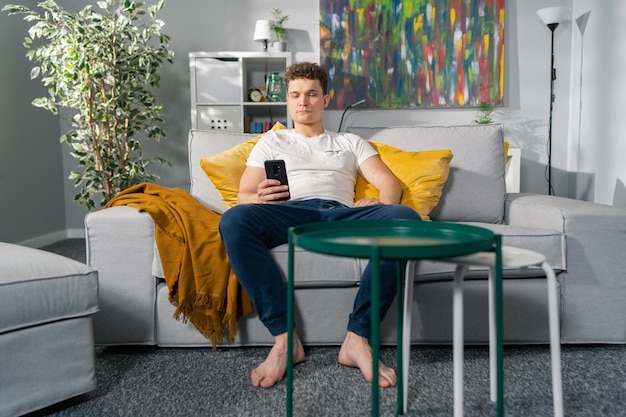 Homem bonito com cabelo encaracolado relaxando no sofá à tarde na sala de estar