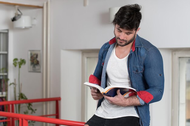 Homem bonito com cabelo escuro em pé na biblioteca Aluno preparando o exame e aprendendo lições na biblioteca escolar