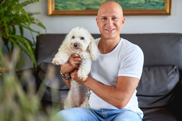 Homem bonito com cachorro branco fofo no sofá