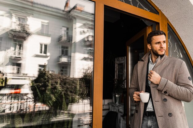 Homem bonito com café posando de casaco no café Estilo de vida masculino