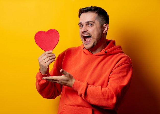 Homem bonito com caixa de forma de coração na parede amarela