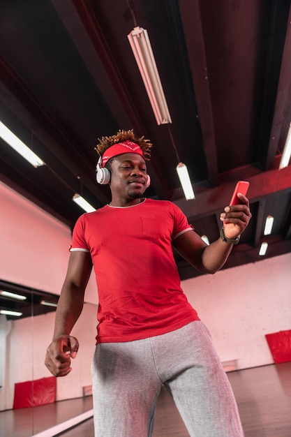 Homem bonito com calça de moletom cinza e segurando o celular enquanto escolhe a música necessária