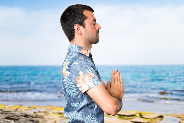 Homem bonito com camisa de flor em posição zen na praia