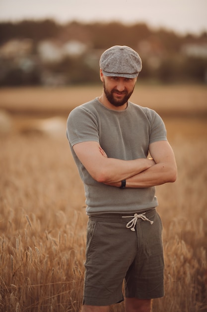 Foto homem bonito com corpo forte e barba escura em camiseta cinza, shorts e boné em um campo de trigo