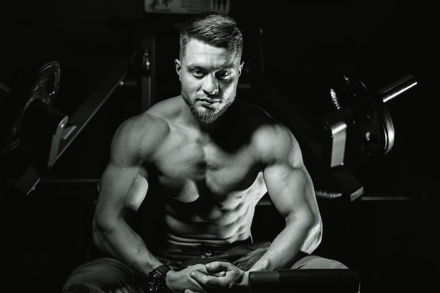 Homem bonito com grandes músculos posando para a câmera no ginásio Fundo preto e azul Retrato de um fisiculturista sorridente Closeup