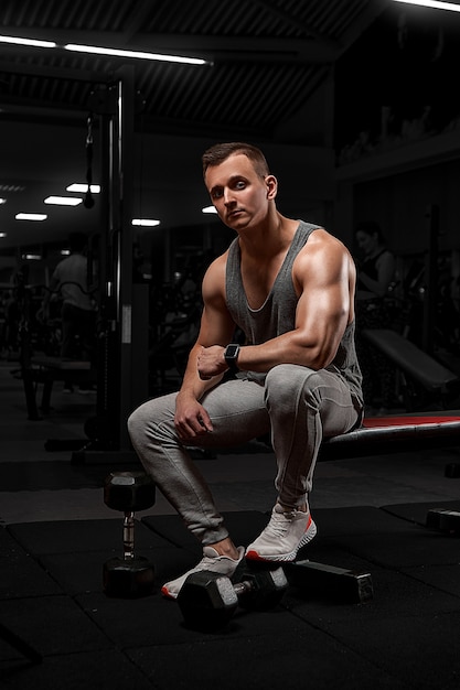 Homem bonito, com grandes músculos, posando para a câmera no ginásio. modelo em sportswear branco