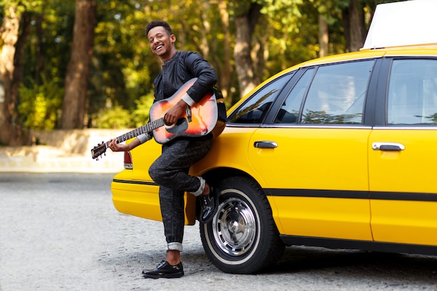 Homem bonito com guitarra perto de táxi amarelo