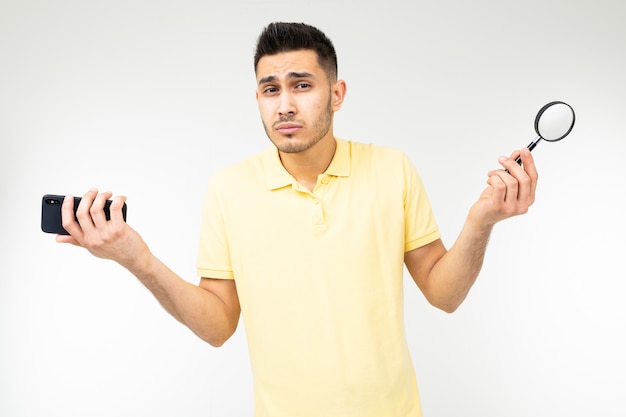 Foto homem bonito com miopia possui uma lupa e um smartphone na mão em um branco com espaço de cópia