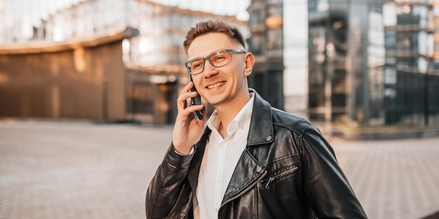 Homem bonito com óculos com um smartphone na rua de uma cidade grande. Empresário falando ao telefone em meio urbano