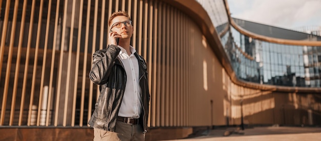 Homem bonito com óculos com um smartphone na rua de uma cidade grande Empresário falando ao telefone em meio urbano