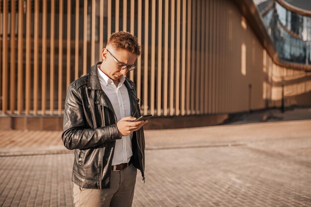 Homem bonito com óculos com um smartphone na rua de uma cidade grande Empresário falando ao telefone em meio urbano