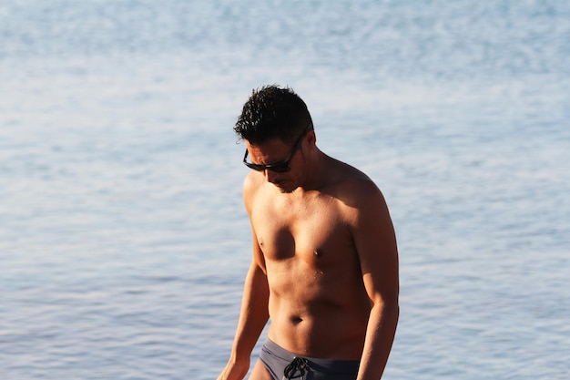 Homem bonito com óculos de sol e maiô está desfrutando na praia ao pôr do sol Apulia Salento Itália