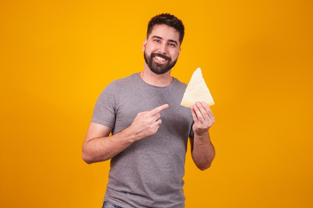 Homem bonito com pedaço de queijo em fundo amarelo. Menino com uma fatia de queijo na mão apontando para ele