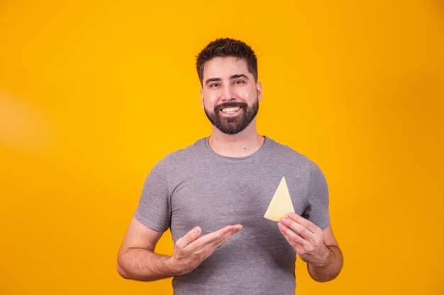 Homem bonito com pedaço de queijo em fundo amarelo. Menino com uma fatia de queijo na mão