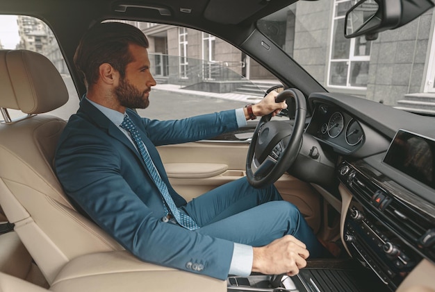 Homem bonito com roupa formal, dirigindo um carro na cidade