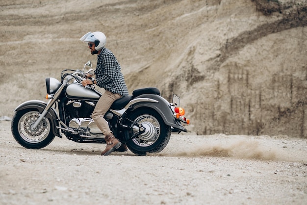 Homem bonito com sua moto na pedreira de areia