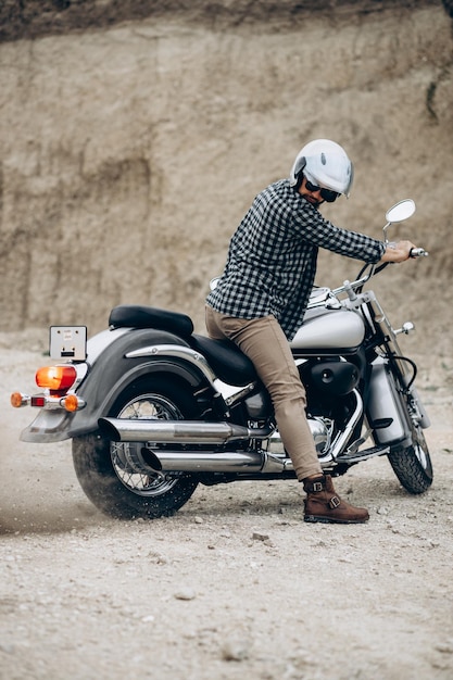 Homem bonito com sua moto na pedreira de areia