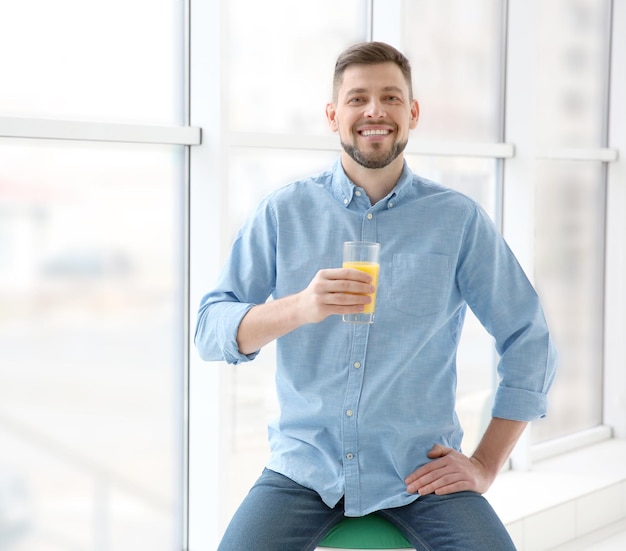 Homem bonito com suco sentado perto da janela