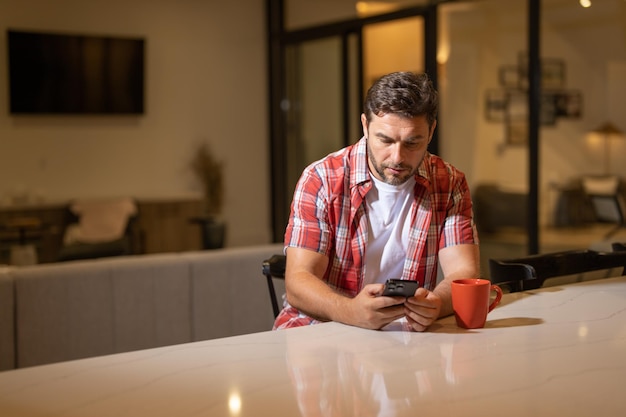 Homem bonito com telefone celular sentado no fim de semana em casa homem americano usando telefone enquanto sentado em