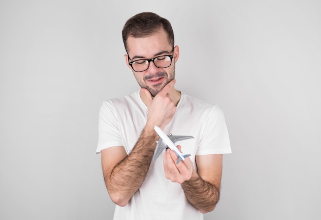 Homem bonito com uma camiseta branca segurando um avião de brinquedo em um fundo cinza