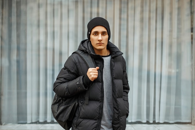 Homem bonito com uma jaqueta preta e um chapéu aconchegante posando perto da janela