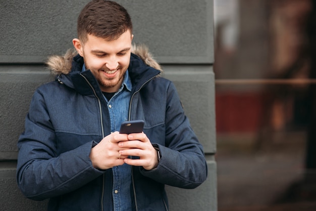 Homem bonito com uma jaqueta usando um telefone parado na rua