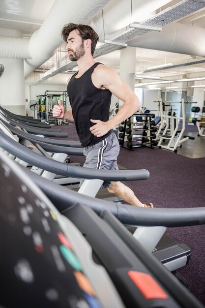 Homem bonito correndo na esteira na academia