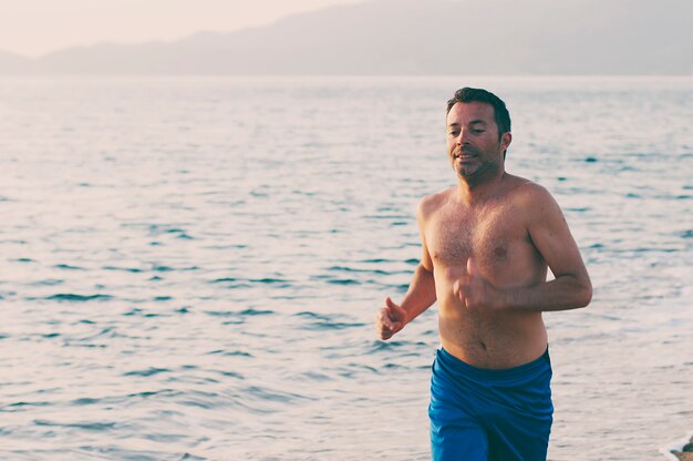 Homem bonito, correndo na praia do sol