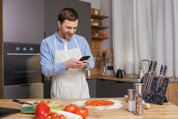 Homem bonito cozinhando na cozinha e fazendo foto preparando comida em seu celular