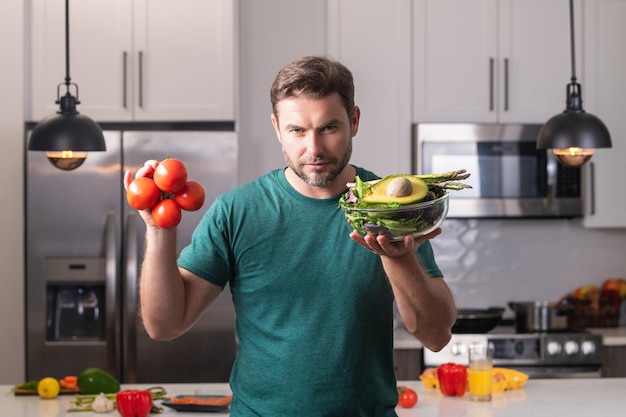 Homem bonito cozinhando salada na cozinha cara cozinhando na cozinha com legumes retrato de homem casual