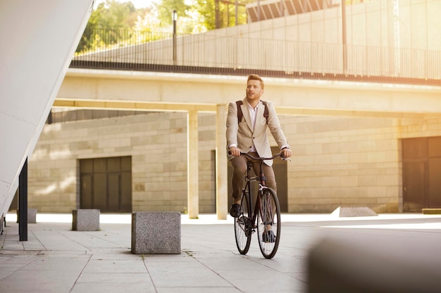 Homem bonito curioso em terno elegante andando de bicicleta e desviar o olhar