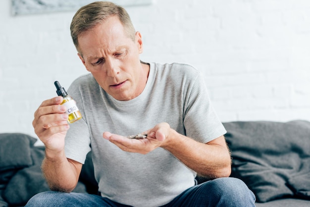 Foto homem bonito de camisa segurando pílulas e óleo de cannabis