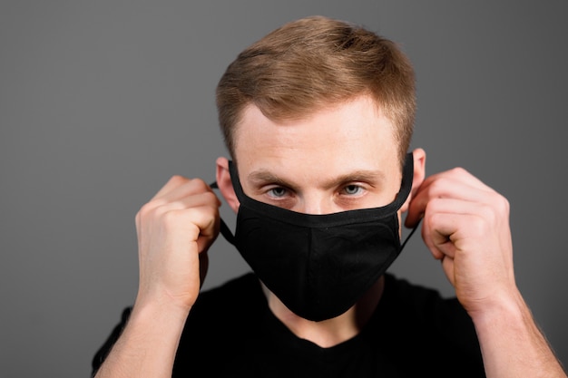 Homem bonito de camiseta preta usar máscara médica preta contra coronavírus em fundo cinza