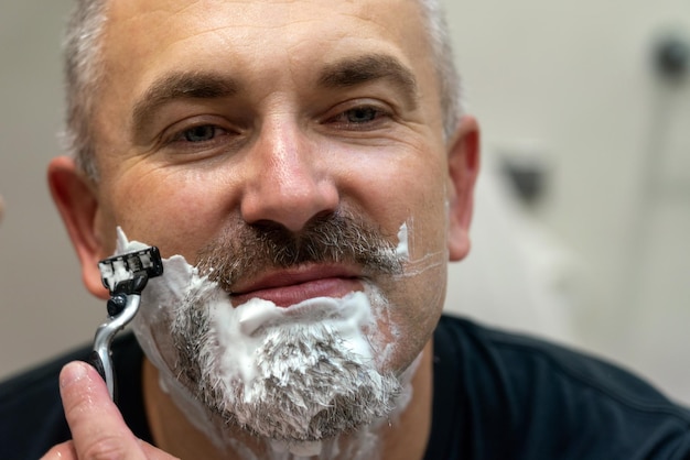 Homem bonito de meia idade, barbear a barba no banheiro